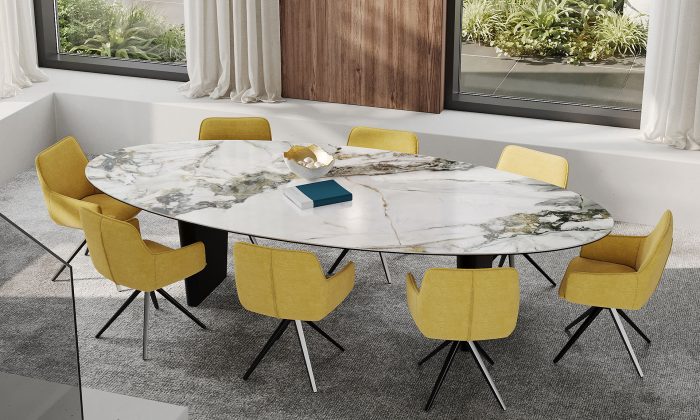 Photo d'ambiance mettant en scène une table de repas ovale avec deux pied en acier laqué noir matte et un plateau en céramique effet marbre. Il y a aussi des chaises jaune pivotantes.